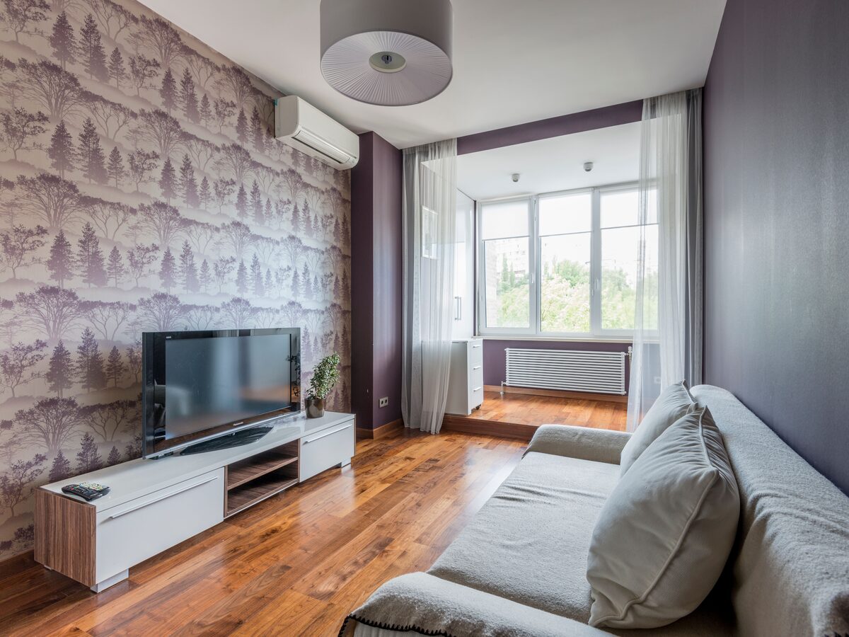 Living room with a mauve toile forest-silhouette accent wall behind the television, hardwood floors and a grey sofa