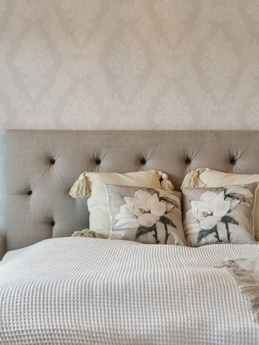 Neutral bedroom with a tufted linen headboard against tone-on-tone beige damask wallpaper