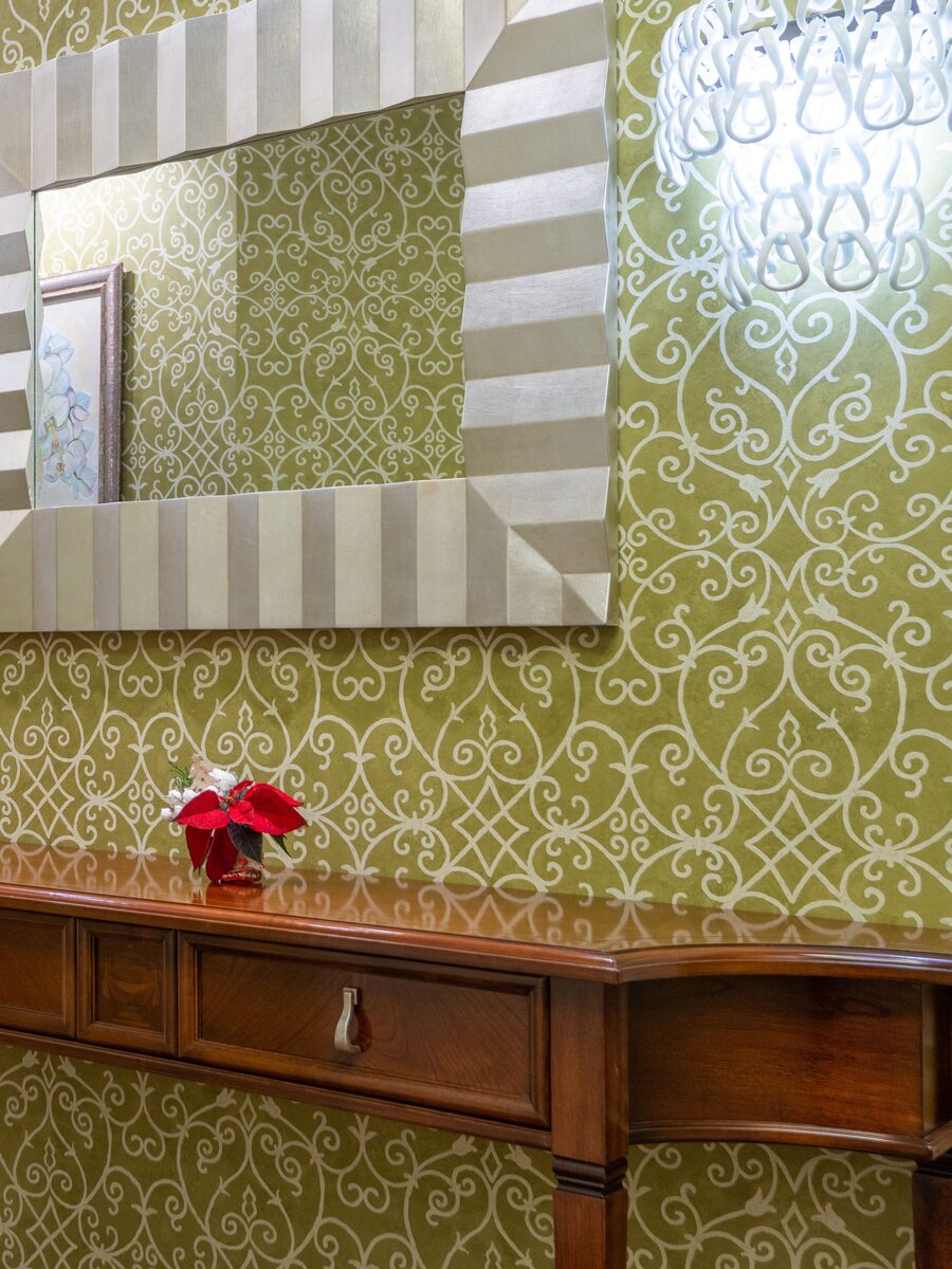 Entry hallway with olive-green scroll wallpaper, a striped silver mirror and a mahogany console table