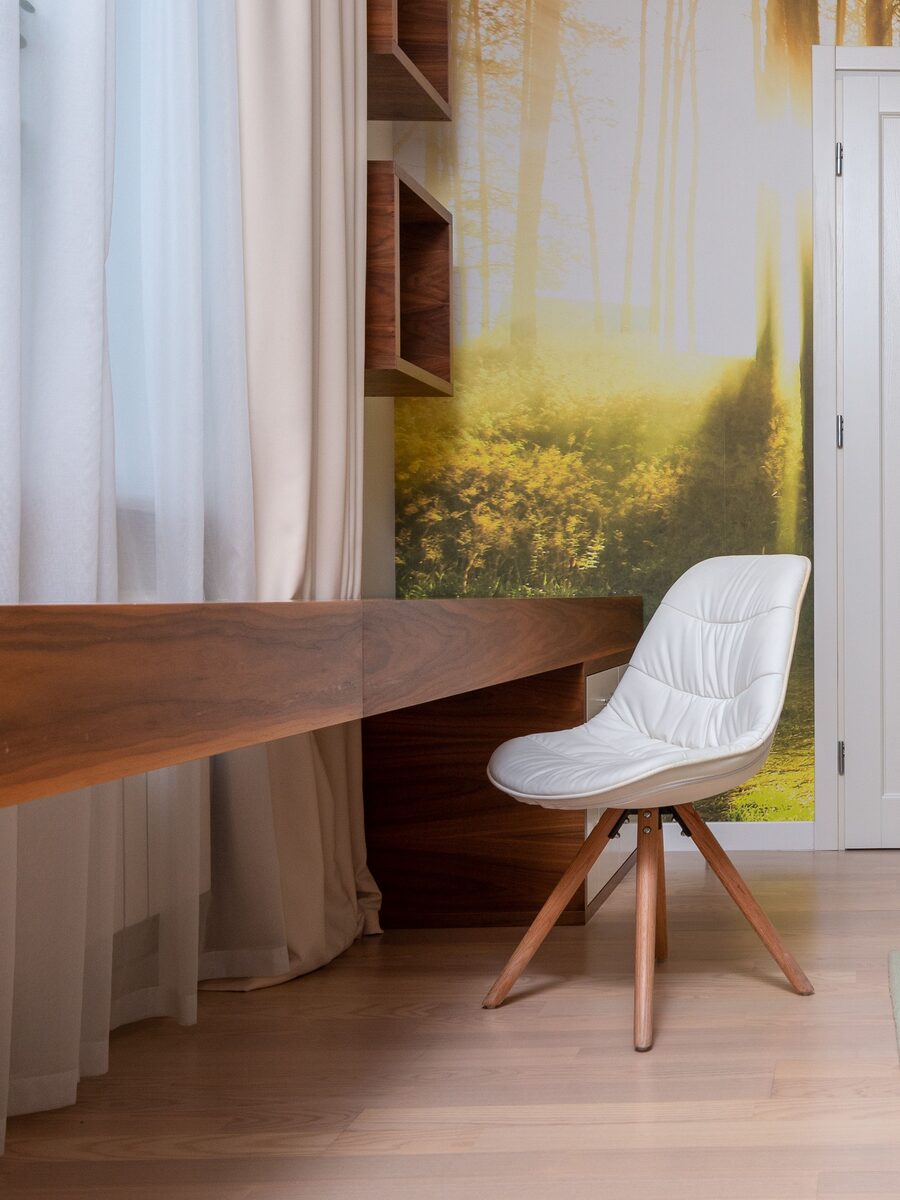 Home office with a walnut desk and white chair in front of a full-wall sunlit forest mural wallpaper