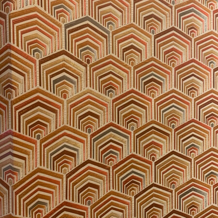 Close-up of an embossed art-deco hexagon wallpaper in terracotta, rust and sand tones on a finished wall